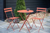 Orange folding table with two matching chairs, set outside.