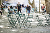 Multiple green folding Bistro tables with chairs, set outdoors.