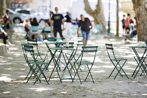Multiple green folding Bistro tables with chairs, set outdoors.