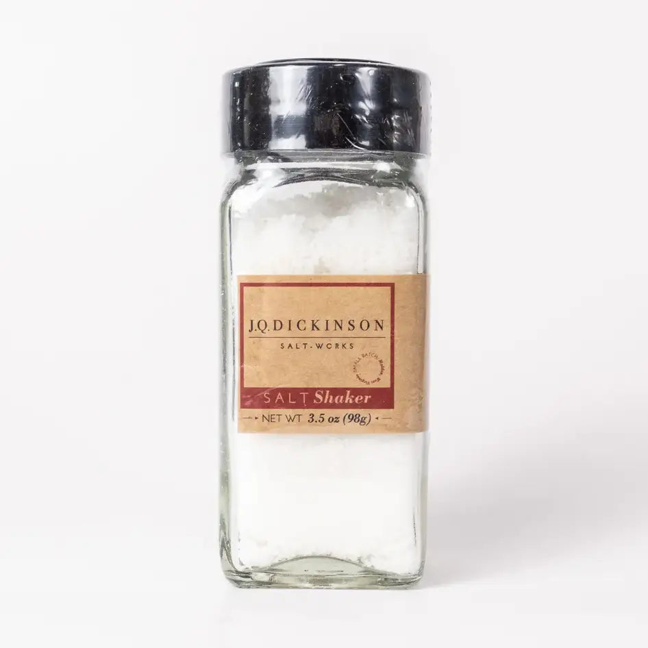 A clear glass spice shaker bottle filled with coarse white salt, featuring a tan paper label with red and black text that reads 'J.Q.