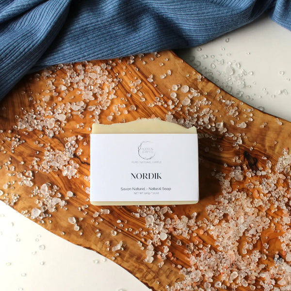 A bar of natural soap with 'ORANGE + PATCHOULI' labeled on the front, placed on a wooden surface with decorative elements around it.