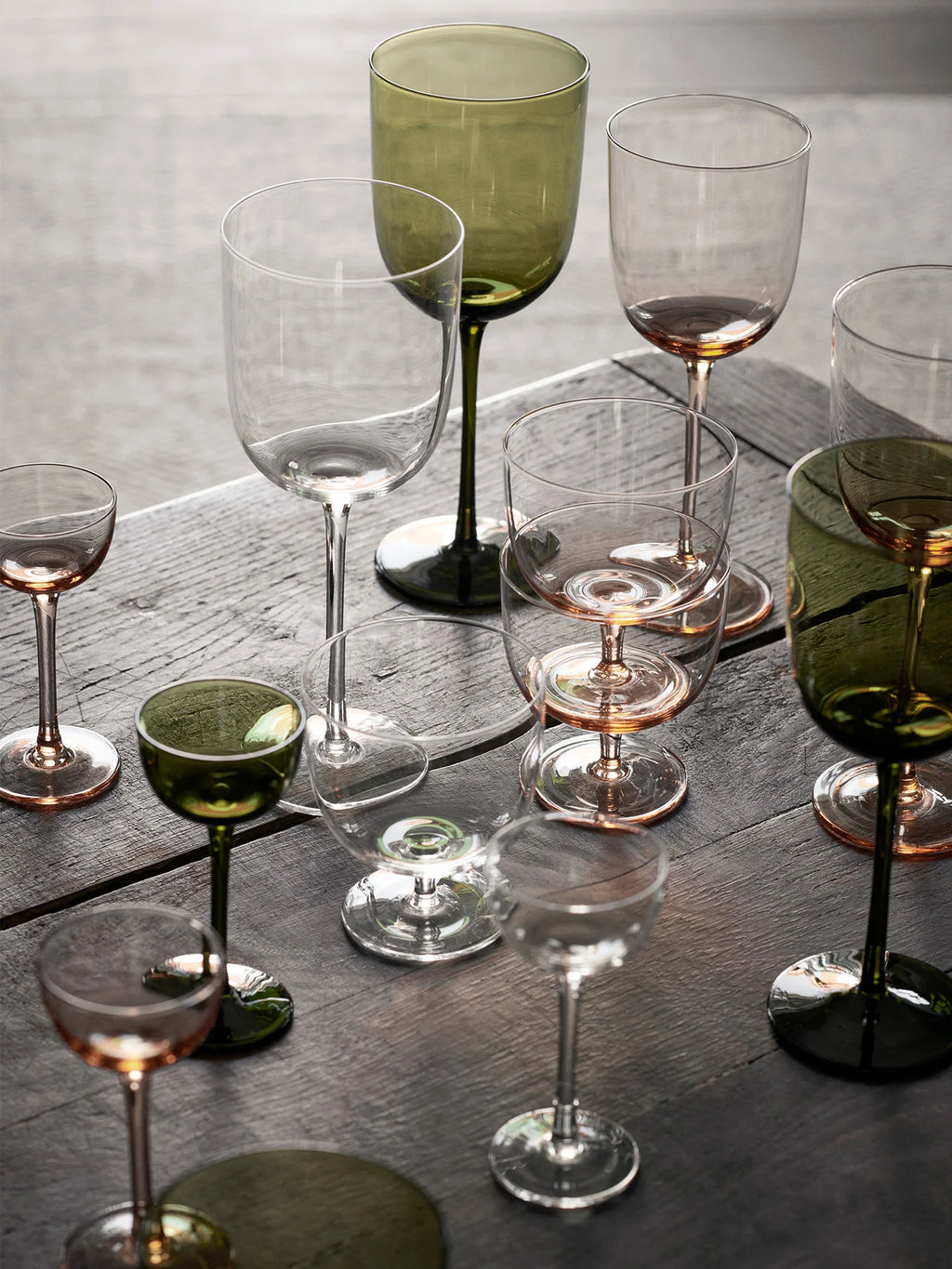 A selection of elegant, mouth-blown glassware including wine glasses, cocktail glasses, and liqueur glasses, displayed on a table. The glassware comes in clear and various colored tints.