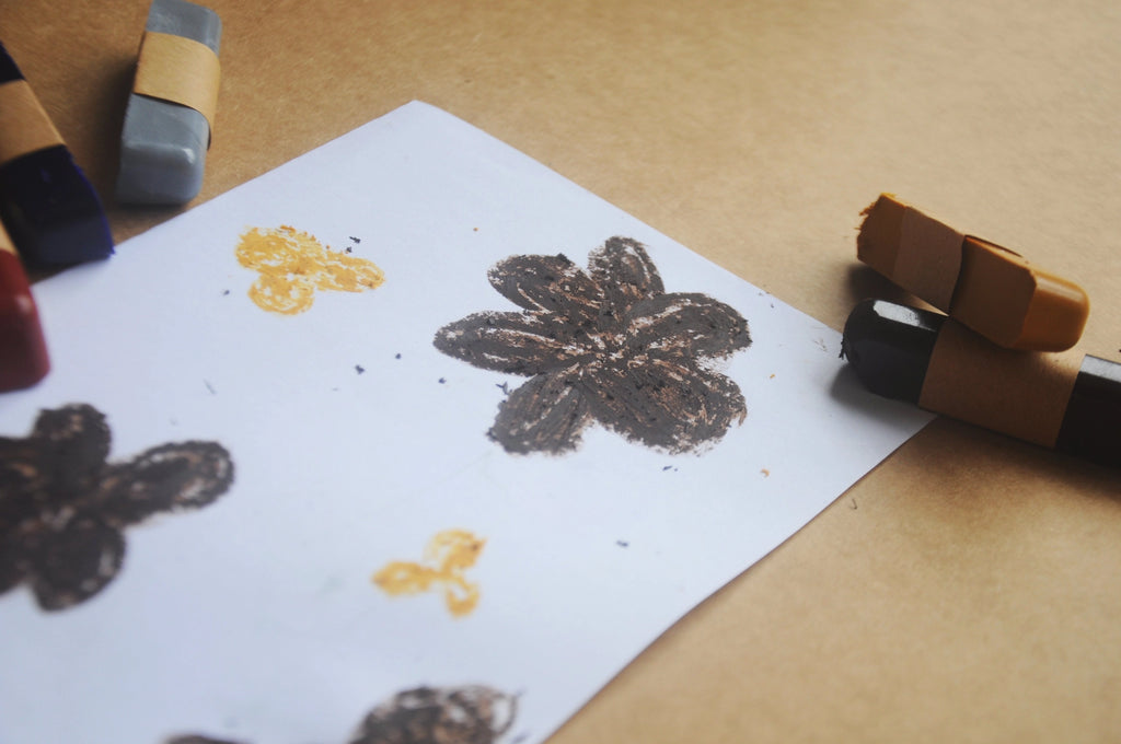 White piece of paper with a drawn brown flower with sticks of pastels