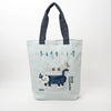 A light blue canvas tote bag with dark navy blue fabric handles, featuring a whimsical winter cat illustration on a clean white background.