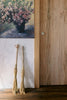 Two brooms leaning against a wooden door with a painting of flowers on the wall.