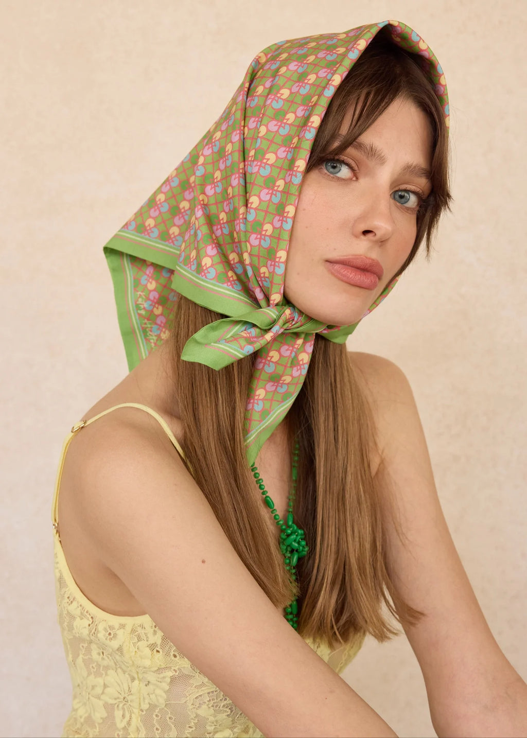Woman wearing a green patterned headscarf on a beige background