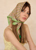 Woman wearing a green patterned headscarf on a beige background