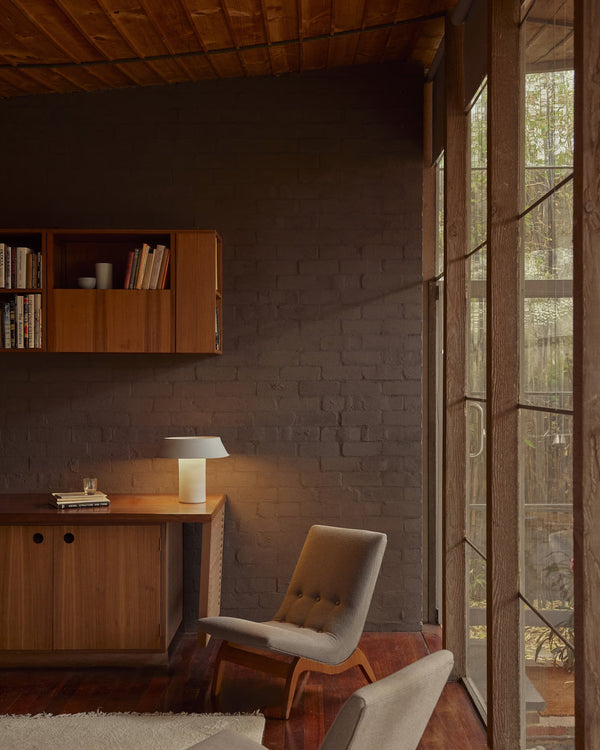 Modern interior with wooden furniture, bookshelf, white lamp and chair near a large window.