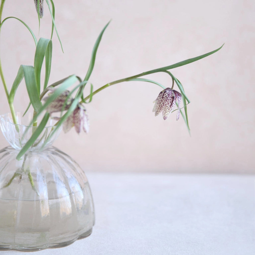 Clear glass vase with green leaves and purple flowers on a light background