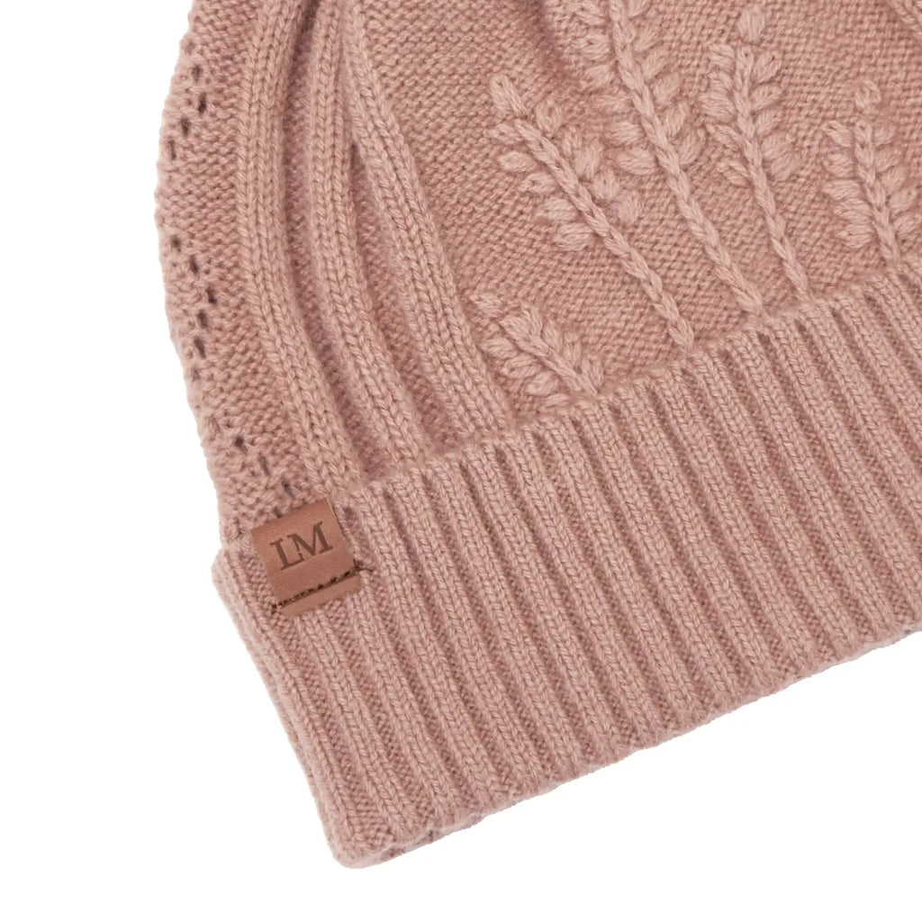Blush pink knitted beanie with cable pattern and brand label on a white background