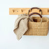 Wicker basket with a towel on a wooden hook rack against a white background