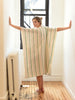 Woman wearing a striped kaftan in a room with a window and radiator.