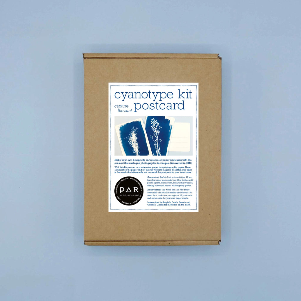 A kraft paper box package labeled 'cyanotype kit capture the postcard' with blue indigo-style postcard designs and a circular 'PAR' seal, centered on a light blue background.