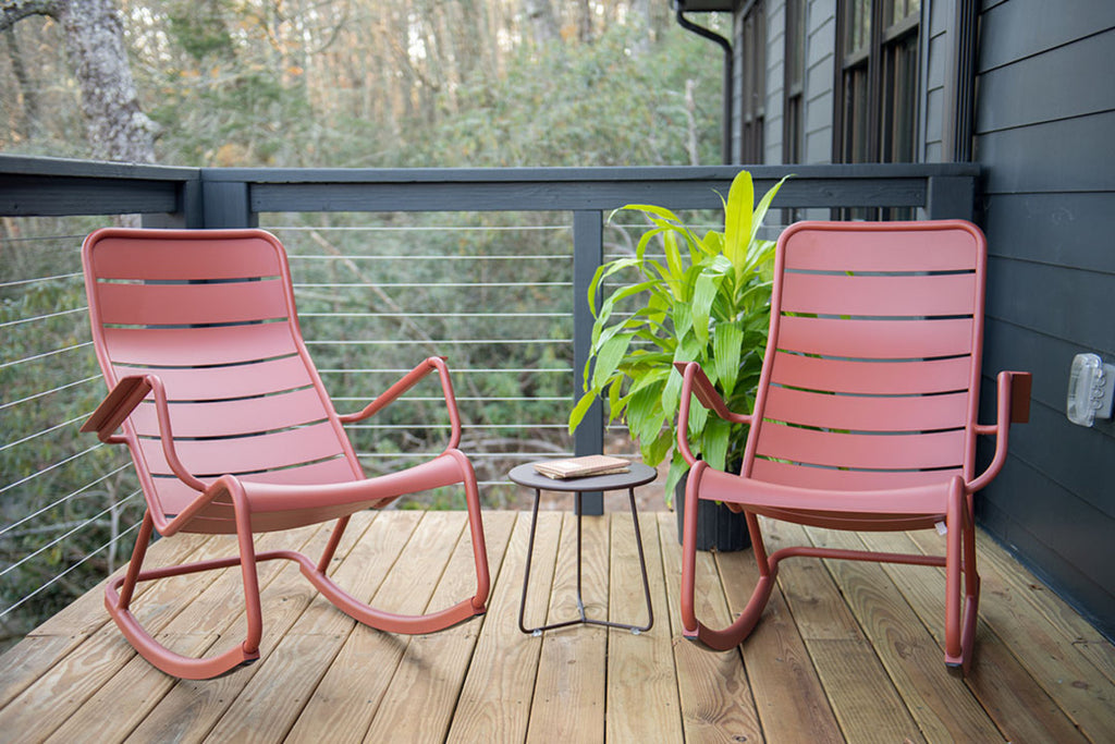 Black side table with geometric base between two red aluminum rocking chairs.