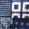 A close-up of a blue and white tie-dye fabric with multiple geometric and circular shibori patterns stitched together.