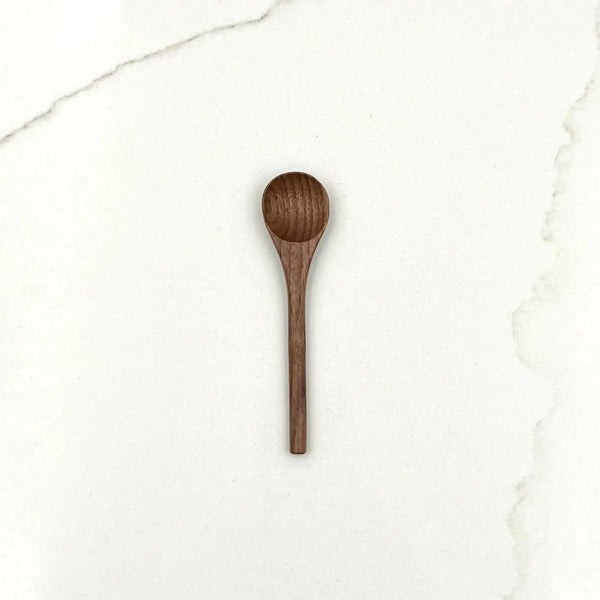 A walnut wood spoon on a white marble surface.