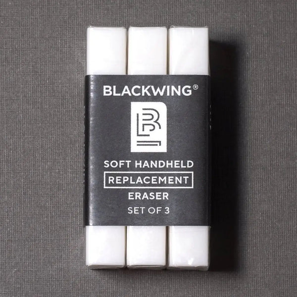 Three white handheld erasers in a black plastic sleeve labeled BLACKWING Soft Handheld Replacement Eraser Set of 3, photographed on a dark gray textured background.
