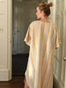 Woman wearing a striped kaftan in a room with white walls and wooden floors.