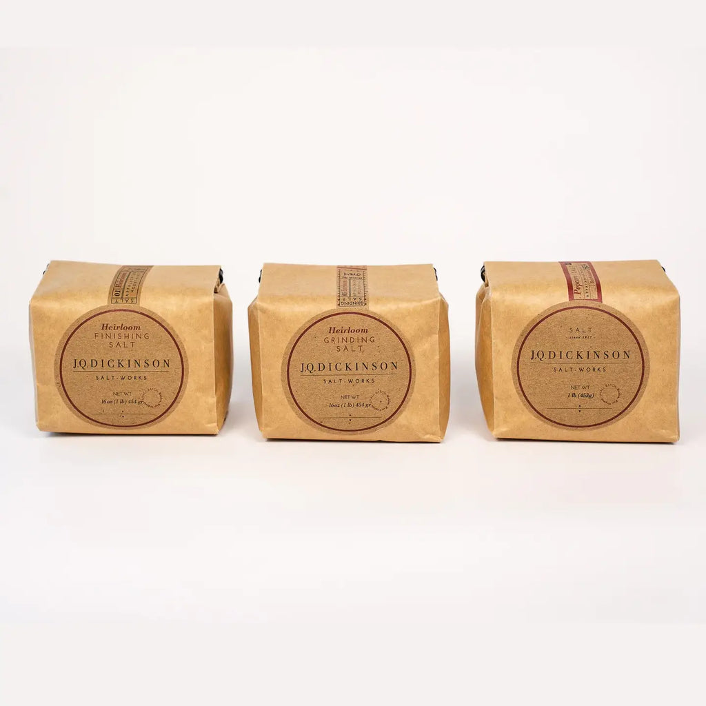 Three square kraft paper packages of J Salt Works sea salt arranged side by side on a clean white background. Q. Dickinson