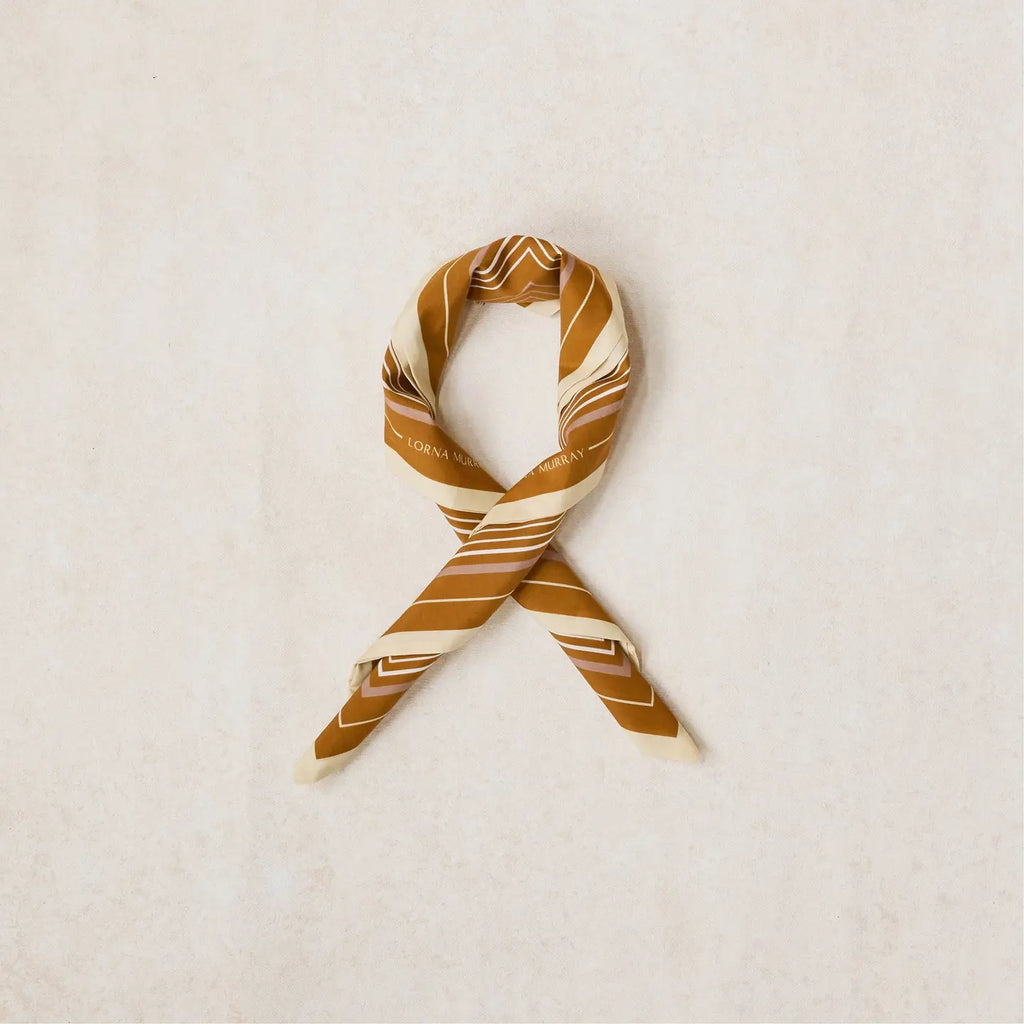 A looped scarf with a geometric stripe pattern in mushroom, rich tan, and clotted cream colors.