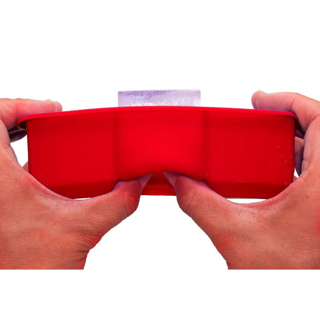 Red ice cube tray held by hands against a white background