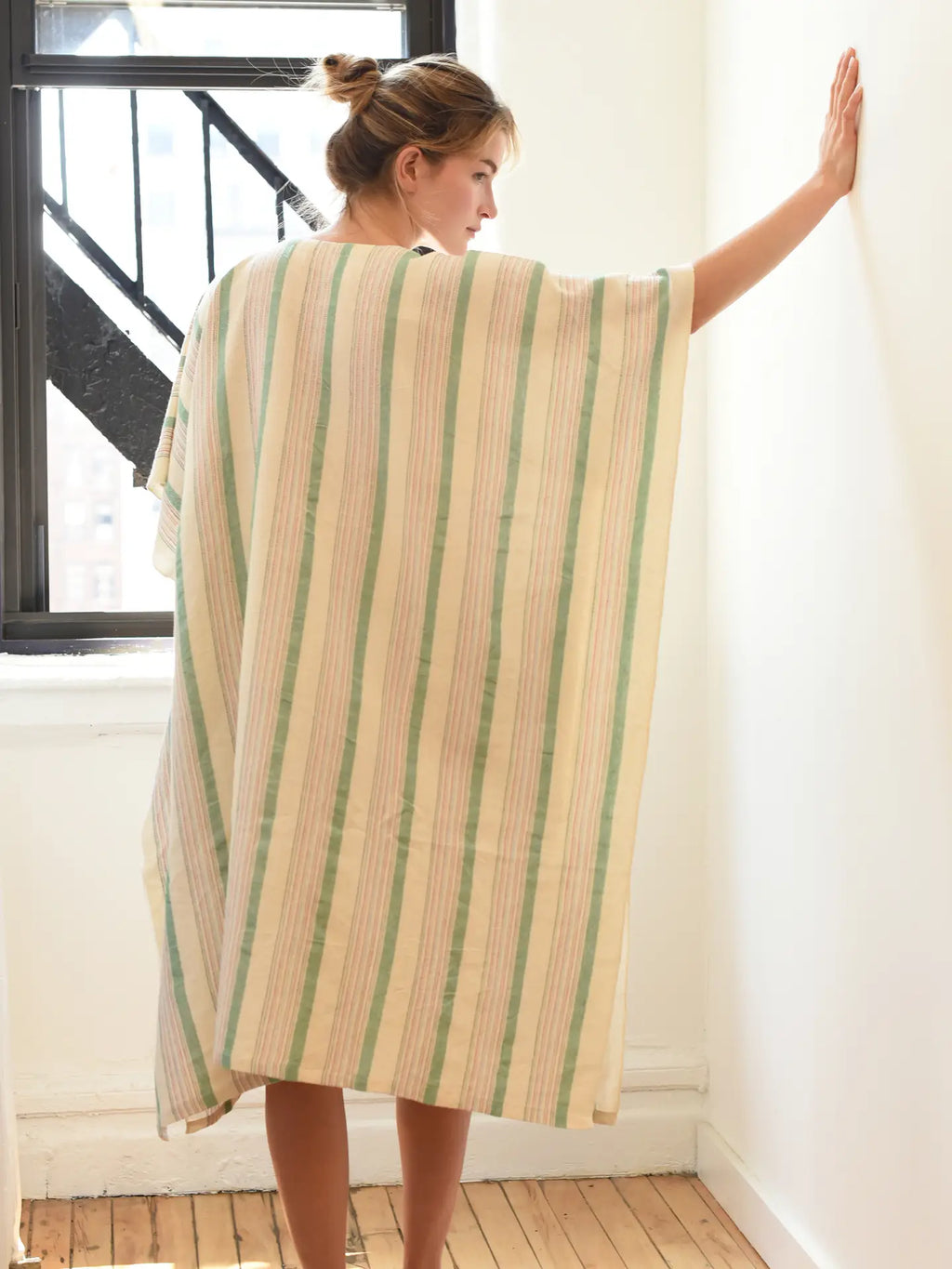 Woman wearing a striped kaftan in a room with a window and wooden floor.