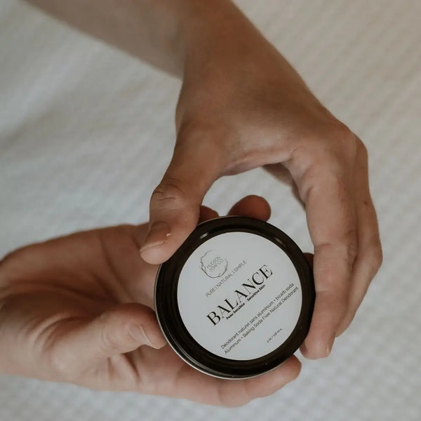 A person holding a container of Balance Sensitive Skin Natural Deodorant with a label that includes the product name and a brief description.
