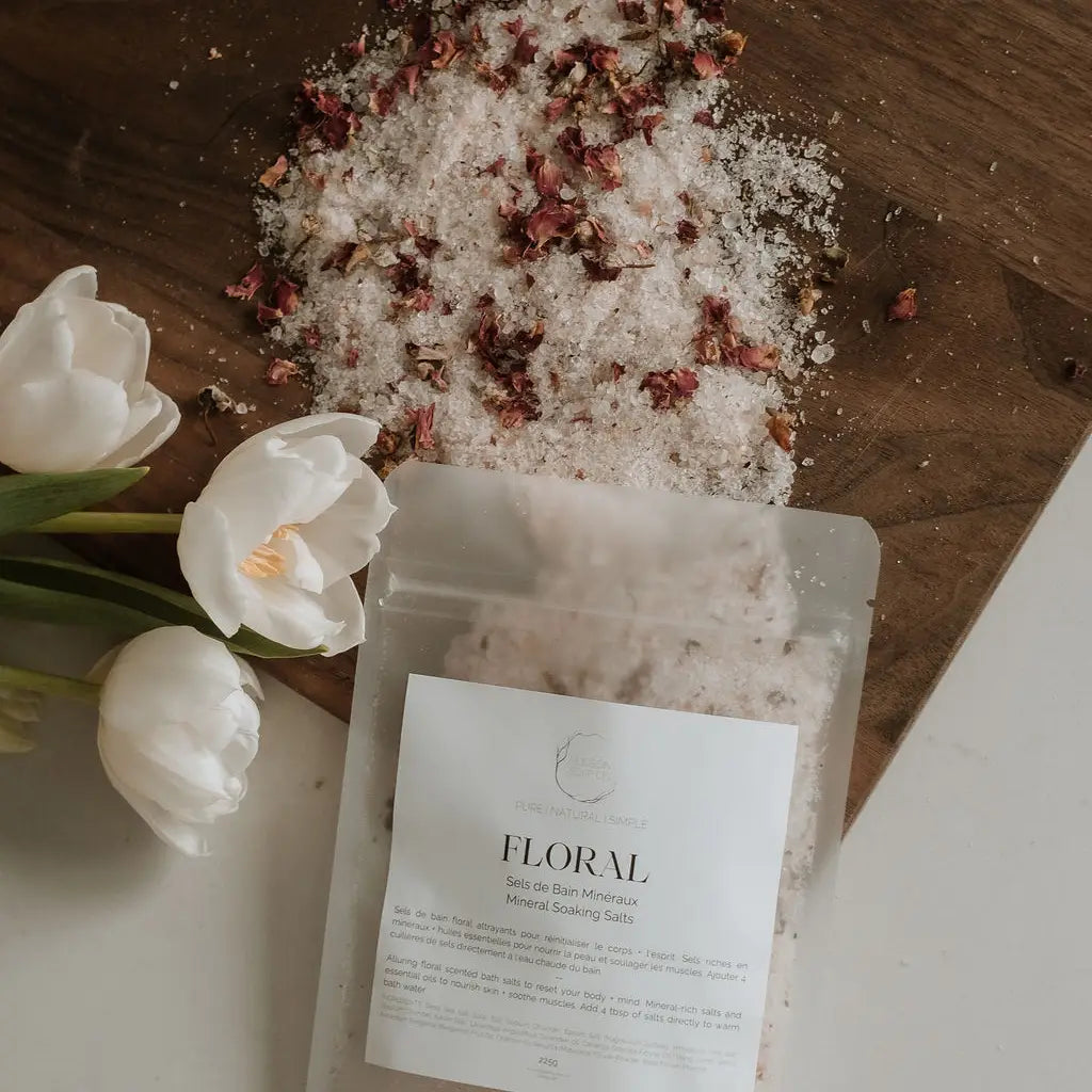 A package of 'Floral' branded soaking salts with lavender essential oil, displayed on a wooden surface with decorative dry plants and white tulips nearby.