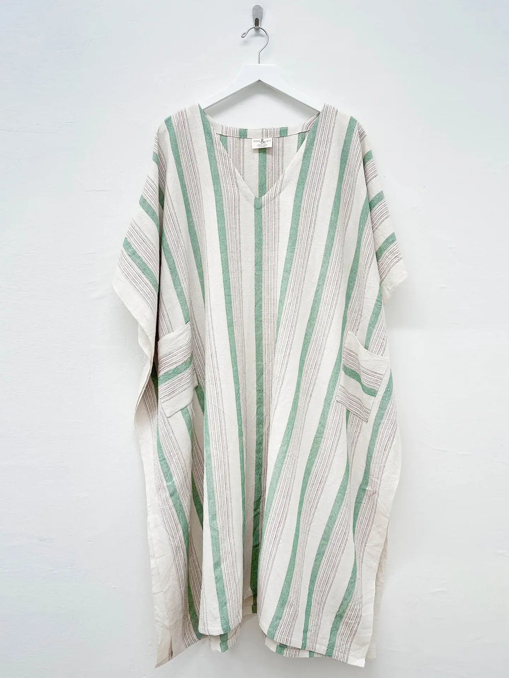 Striped kaftan with green and white pattern on a hanger against a white background
