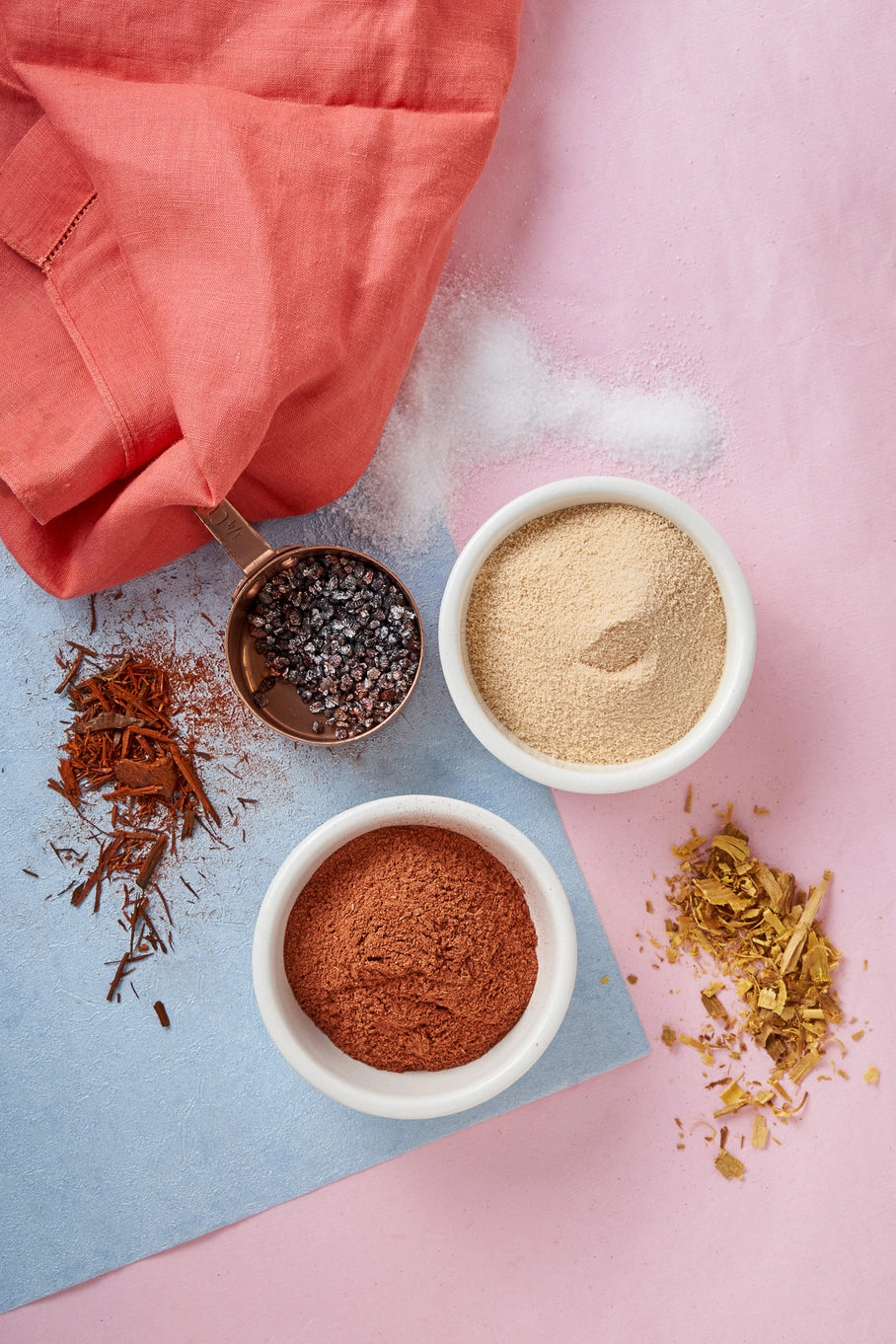 Three small bowls with different powders on a pink and blue background