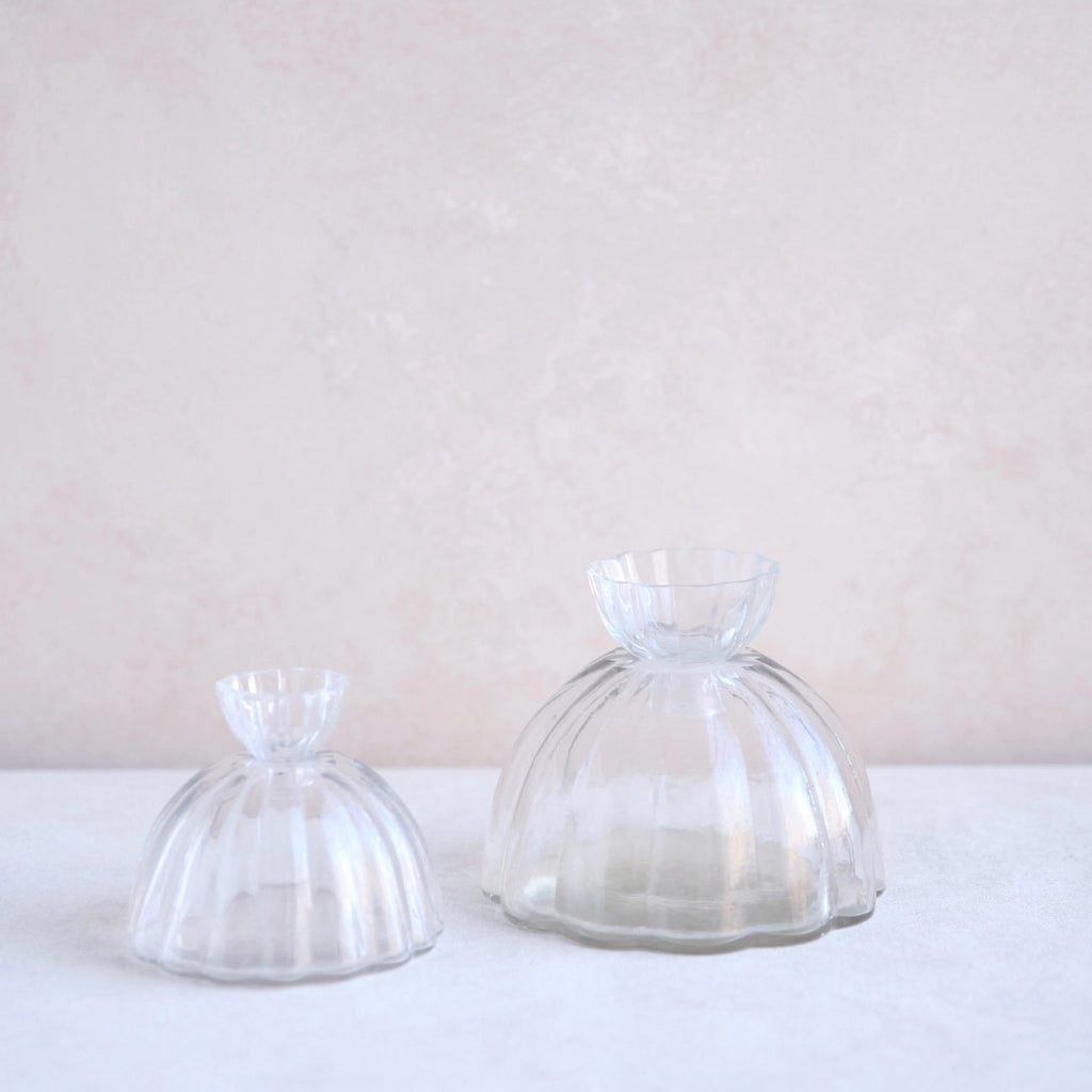 Two clear glass dome-shaped items on a white surface with a light pink background