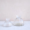 Two clear glass dome-shaped items on a white surface with a light pink background