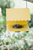 Yellow bird feeder with seeds hanging against a blurred green background