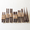 A selection of hand-poured taper candles in various shapes and sizes, all in a dark brown/espresso color, displayed against a neutral background.
