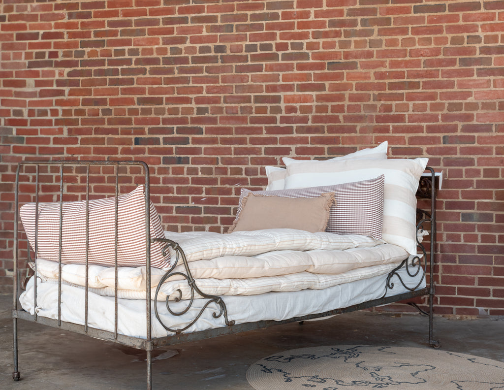 A white cotton mattress topper displayed on a bed with a metal frame, against a brick wall background.