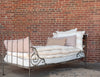 A white cotton mattress topper displayed on a bed with a metal frame, against a brick wall background.