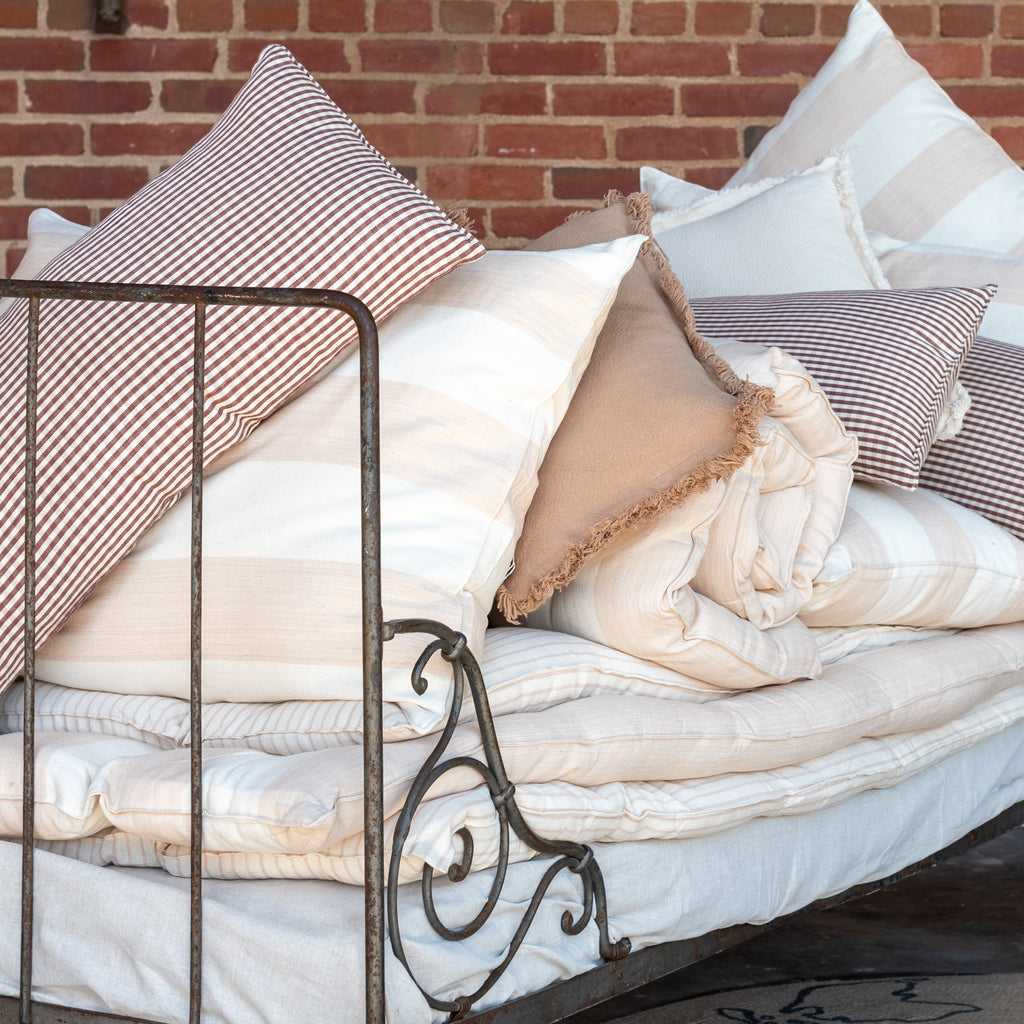 A close up view of a white cotton mattress topper displayed on a bed with a metal frame, against a brick wall background.