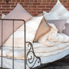 A close up view of a white cotton mattress topper displayed on a bed with a metal frame, against a brick wall background.