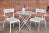 Two white Luxembourg armchairs, placed on either side of a round table, against a brick wall background.