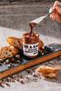 Chocolate hazelnut butter being spread on bread with a jar labeled 'Fine & Raw' in the background.
