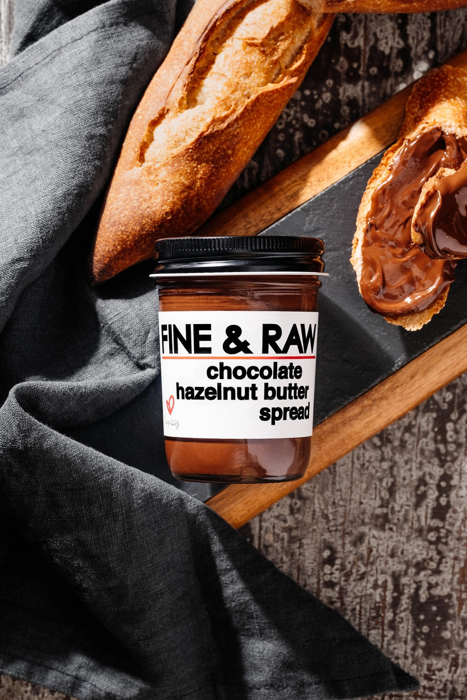Jar of Fine & Raw chocolate hazelnut butter spread with bread on a wooden board.