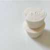 Two stacked white soaps with engraved letters on a light gray background