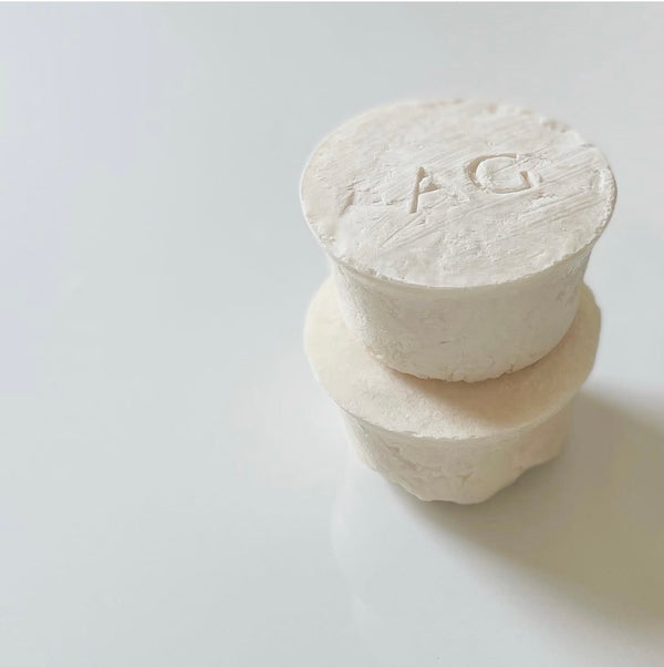 Two stacked white soaps with engraved letters on a light gray background