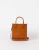 A brown leather tote bag with a structured silhouette, featuring a white and red adjustable strap, two handles, and a minimalist latch closure.