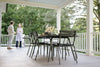 A family enjoying a meal at a Fermob Luxembourg Pedestal Table on a porch with greenery in the background.