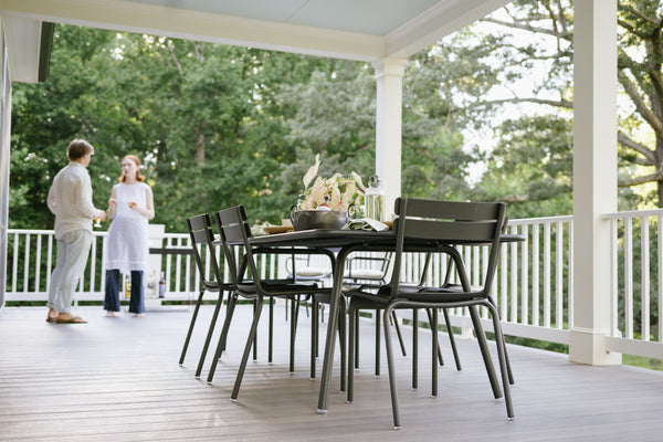 A family enjoying a meal at a Fermob Luxembourg Pedestal Table on a porch with greenery in the background.