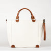 A blanc cotton tote bag with brown leather handles and a removable brown leather strap, featuring a zippered closure and an interior pocket, set against a white background.