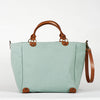 A menthe seafoam cotton tote bag with brown leather handles and a removable brown leather strap, featuring a zippered closure and an interior pocket, set against a white background, side view.