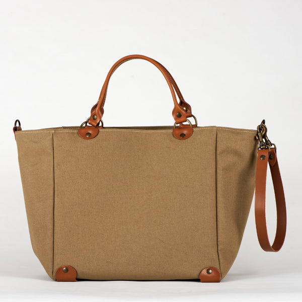 A beige cotton tote bag with brown leather handles and a removable brown leather strap, featuring a zippered closure and an interior pocket, set against a white background.