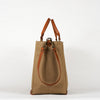 A beige cotton tote bag with brown leather handles and a removable brown leather strap, featuring a zippered closure and an interior pocket, set against a white background, side view.